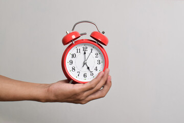 Vintage red alarm clock in hand. Round red alarm clock isolated on white background shows 5 am
