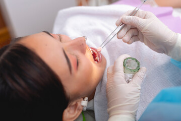 A dental professional applying a medicated cotton pellet to the patient's gums using tweezers. The patient lies back, relaxed, while the dentist wears gloves for a hygienic procedure.