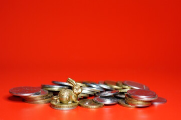 Naklejka premium A metal rabbit figurine with coins on a red background.