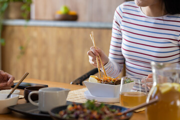 At home, Eating asian cuisine, young woman using chopsticks at dining table with family