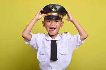 Little Asian boy Beaming airplane pilot holding hat in arms isolated on yellow background. Little boy dreams of becoming an airplane pilot.