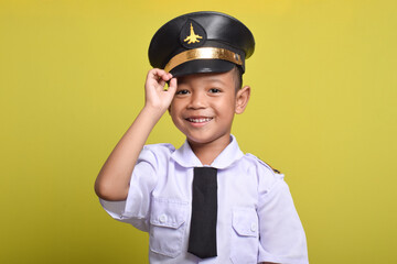 Little Asian boy Beaming airplane pilot holding hat in arms isolated on yellow background. Little boy dreams of becoming an airplane pilot.