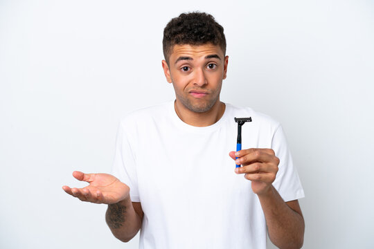 Young Brazilian man shaving his beard isolated on white background making doubts gesture while lifting the shoulders