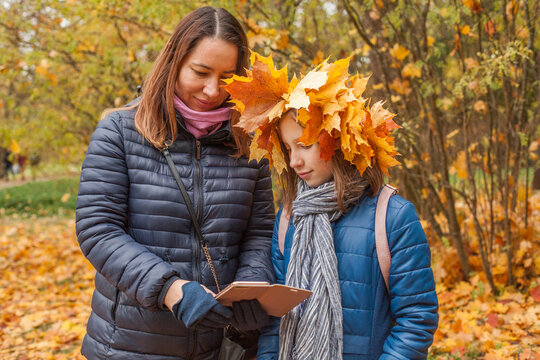 Portrait of mother and daughter holding smartphone in autumn park background