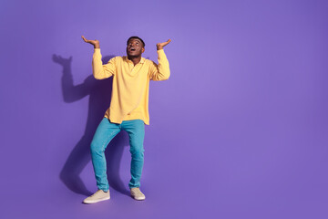 Full length photo of handsome young guy look up empty space hold ceiling dressed stylish yellow garment isolated on violet color background