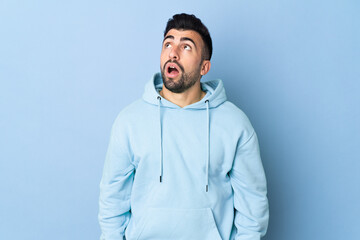 Caucasian man over isolated blue background looking up and with surprised expression