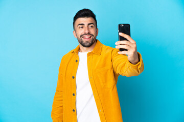 Caucasian man over isolated blue background making a selfie with mobile phone