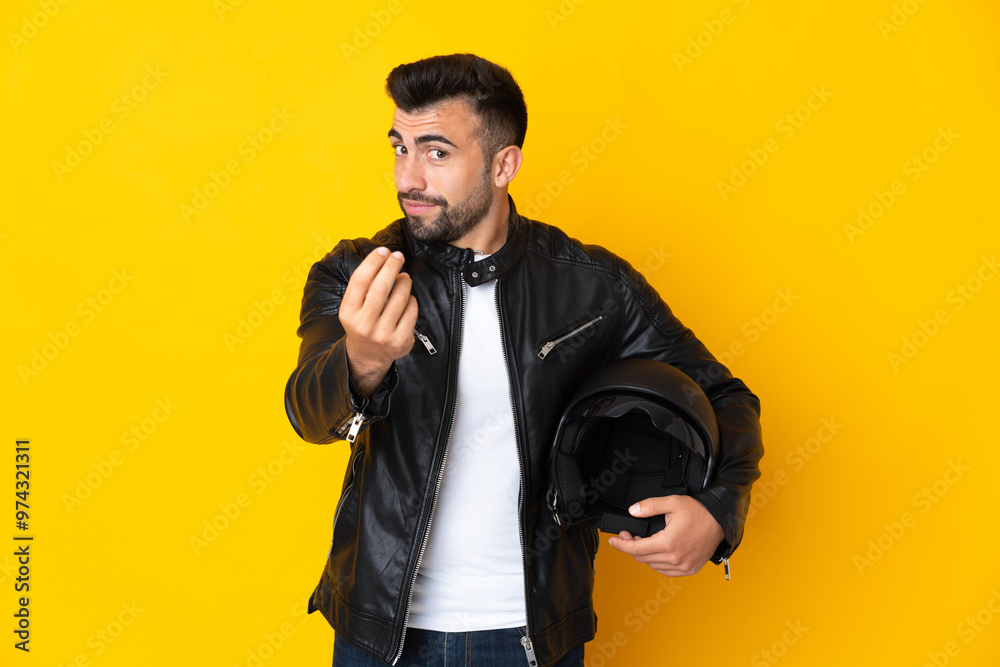 Wall mural caucasian man with a motorcycle helmet over isolated yellow background making money gesture