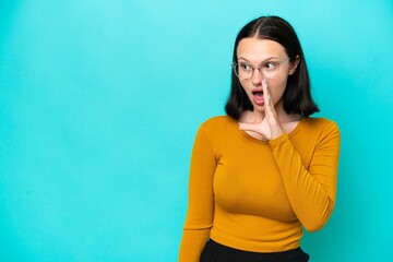 Young caucasian woman isolated on blue background whispering something with surprise gesture while looking to the side