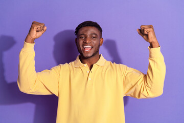 Photo portrait of attractive young man winning raise fists dressed stylish yellow clothes isolated on violet color background