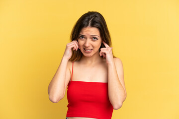 Young caucasian woman isolated on yellow background frustrated and covering ears