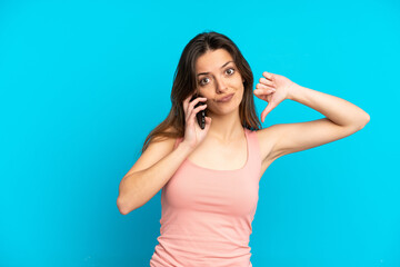 Fototapeta premium Young caucasian woman using mobile phone isolated on blue background showing thumb down with negative expression