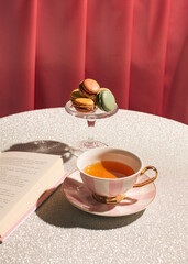 A cup of tea, macarons and a book on a table, 