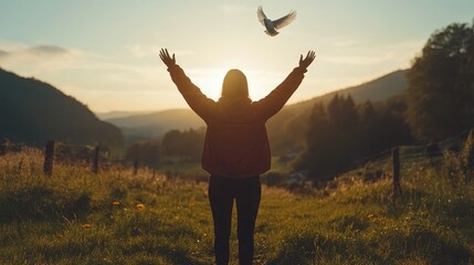 A person standing in an open field with hands raised in prayer, as a white dove soars into the bright blue sky, symbolizing freedom and peace