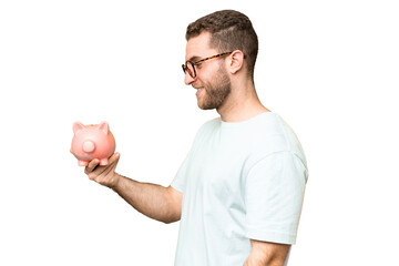 Young man holding a piggybank over isolated chroma key background with happy expression