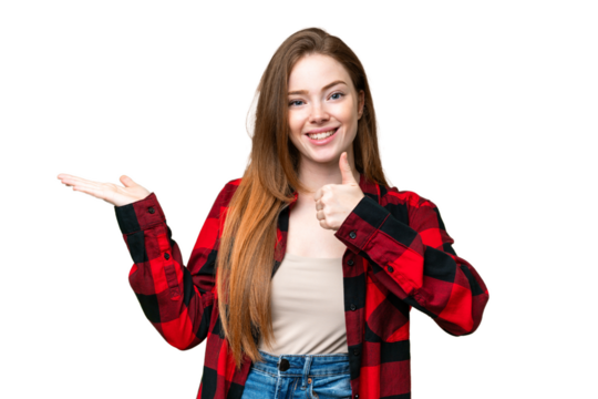 Young pretty woman over isolated chroma key background holding copyspace imaginary on the palm to insert an ad and with thumbs up