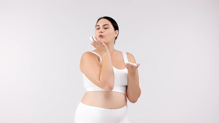 Fototapeta premium Young, beautiful brunette with curvy figure using skincare products on a white background. Perfect for promoting skincare, emphasizing confidence and beauty with your products.