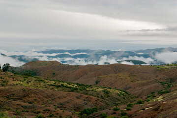 Rolling clouds drift over rugged mountains, barren hills contrast against the sky in high altitude peaks and valleys, showcasing untouched nature in green, brown, and blue hues