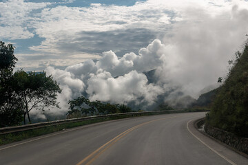 Foggy mountain road disappears into clouds, creating a mysterious atmosphere. The scenic route offers a breathtaking view, perfect for a drive through the misty weather, inspiring awe and wonder