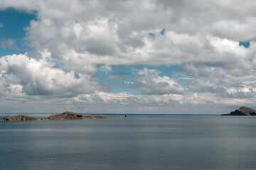 Lake titicaca is displaying its intense blue color below a partly cloudy sky with small, rocky islands dotting the horizon