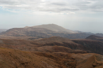 Naklejka premium Layers of mountains are creating a beautiful scenery in a remote area. The brown color of the soil is contrasting with the cloudy sky