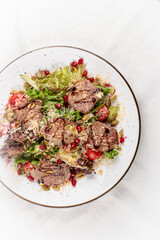 A fresh salad featuring tender veal, juicy cherry tomatoes, and crunchy pomegranate seeds.