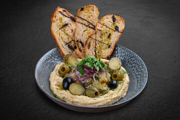 Roasted eggplant hummus served with olives, pickled cucumbers, and croutons. This Mediterranean-inspired dish.