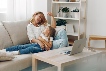 Mother and child enjoying quality time on the couch with a laptop and coffee table in a cozy living...