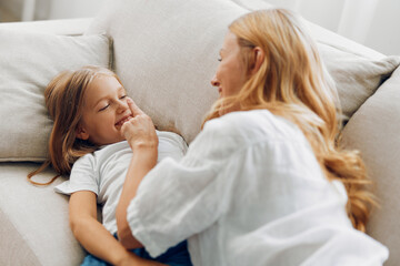 Heartwarming moment of a mother and daughter sharing a tender touch while sitting together on a cozy couch