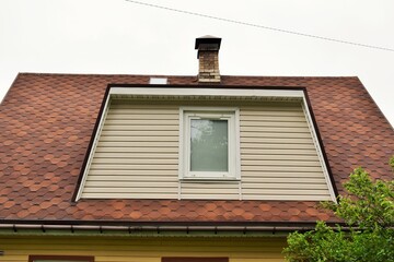 A window on the attic floor of a residential building and a brick chimney on the roof