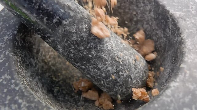 Large pieces of the sweet brown sugar are falling into the grey stone mortar in slow motion. High quality 4k footage