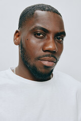 Obraz premium Portrait of a male model with a neutral expression, wearing a white t shirt, set against a light gray background, highlighting modern fashion and self confidence
