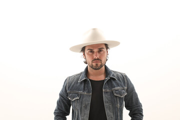 Fototapeta premium Bearded young man wearing denim jacket and fedora hat over white wall. 