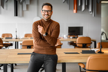 Handsome young professional in eyeglasses smiling and looking at camera while sitting in meeting room