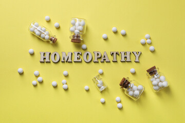Word Homeopathy and pills on pale yellow background, flat lay