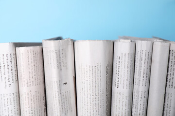 Many newspapers in different languages on light blue background, closeup