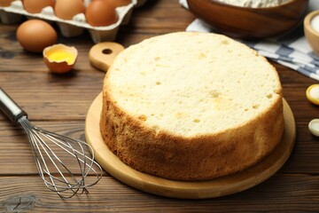 Tasty cut sponge cake, whisk and ingredients on wooden table