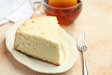 Piece of delicious sponge cake served on beige textured table, closeup