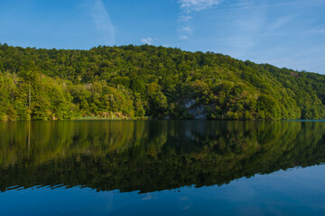 Fototapeta premium A peaceful morning unfolds at Plitvice Lakes, where lush greenery surrounds still waters, creating stunning reflections
