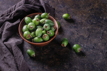 Tropical fruits green ripe feijoa sellowiana berries in a clay bowl and on a table on a dark background with copy space for text
