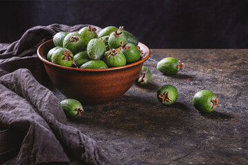 Tropical fruits green ripe feijoa sellowiana berries in a clay bowl and on a table on a dark background with copy space for text