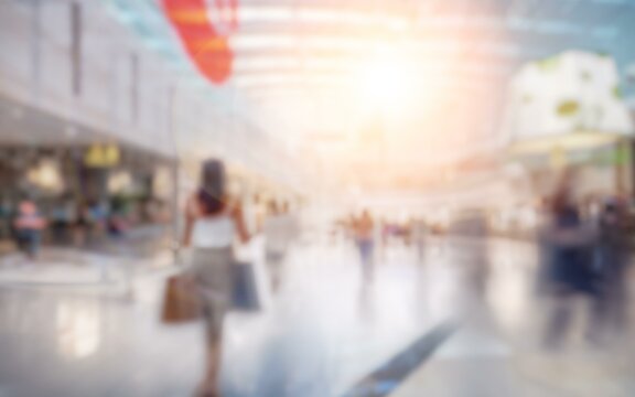 A blurry view of a shopping mall with people walking around. The background has bokeh and bright light.
