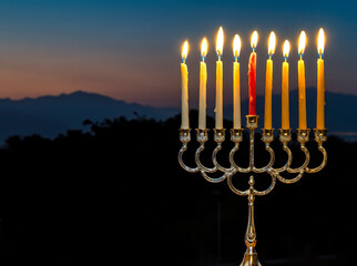 Fototapeta premium Burning Hanukkah candles as Jewish Holiday of Light, the original photo was taken against the backdrop of the sunset in the mountains, selective focus on the candle flames, no AI tools were used
