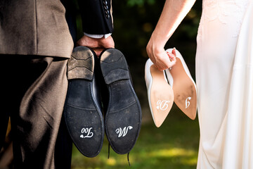 Close-up of bride and groom holding their wedding shoes with handwritten messages 'I do' and 'Me too' on the soles. Unique wedding detail capturing the couple's commitment. 