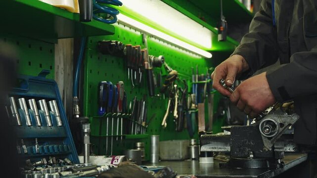 Auto mechanic repairs auto part steering rack in a large workshop filled with various tools hanging on the walls