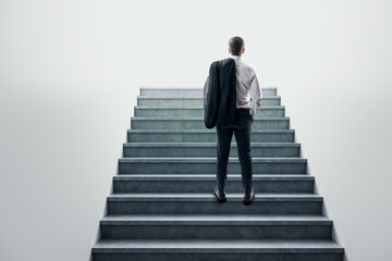 Businessman standing at the base of a concrete staircase, looking up.