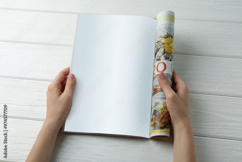 Wall mural Woman reading magazine at white wooden table, closeup. Mockup for design