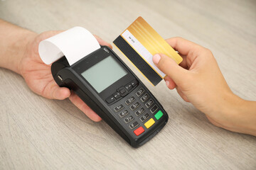 Man taking payment from client via credit card terminal at wooden table, closeup