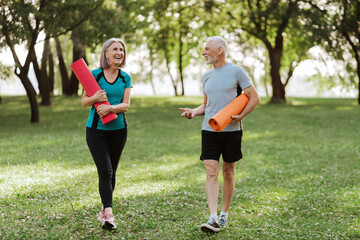 Senior couple walking through park holding yoga mats after outdoor workout