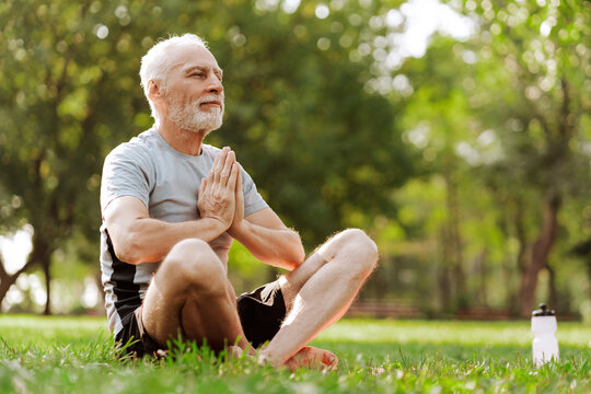 Senior man practicing yoga meditation outdoors in park outdoors